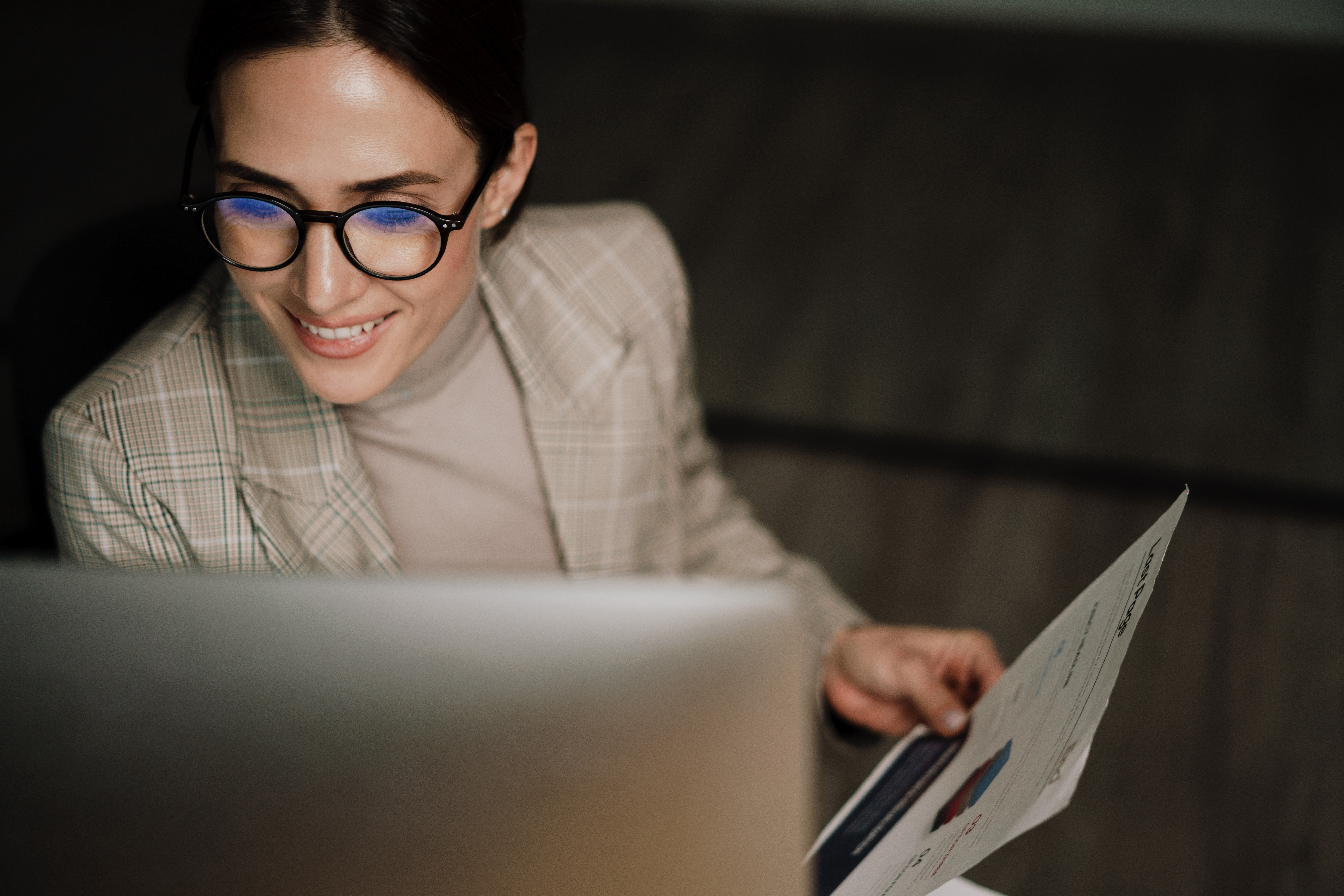 A woman holding files sitting in front of a computer.