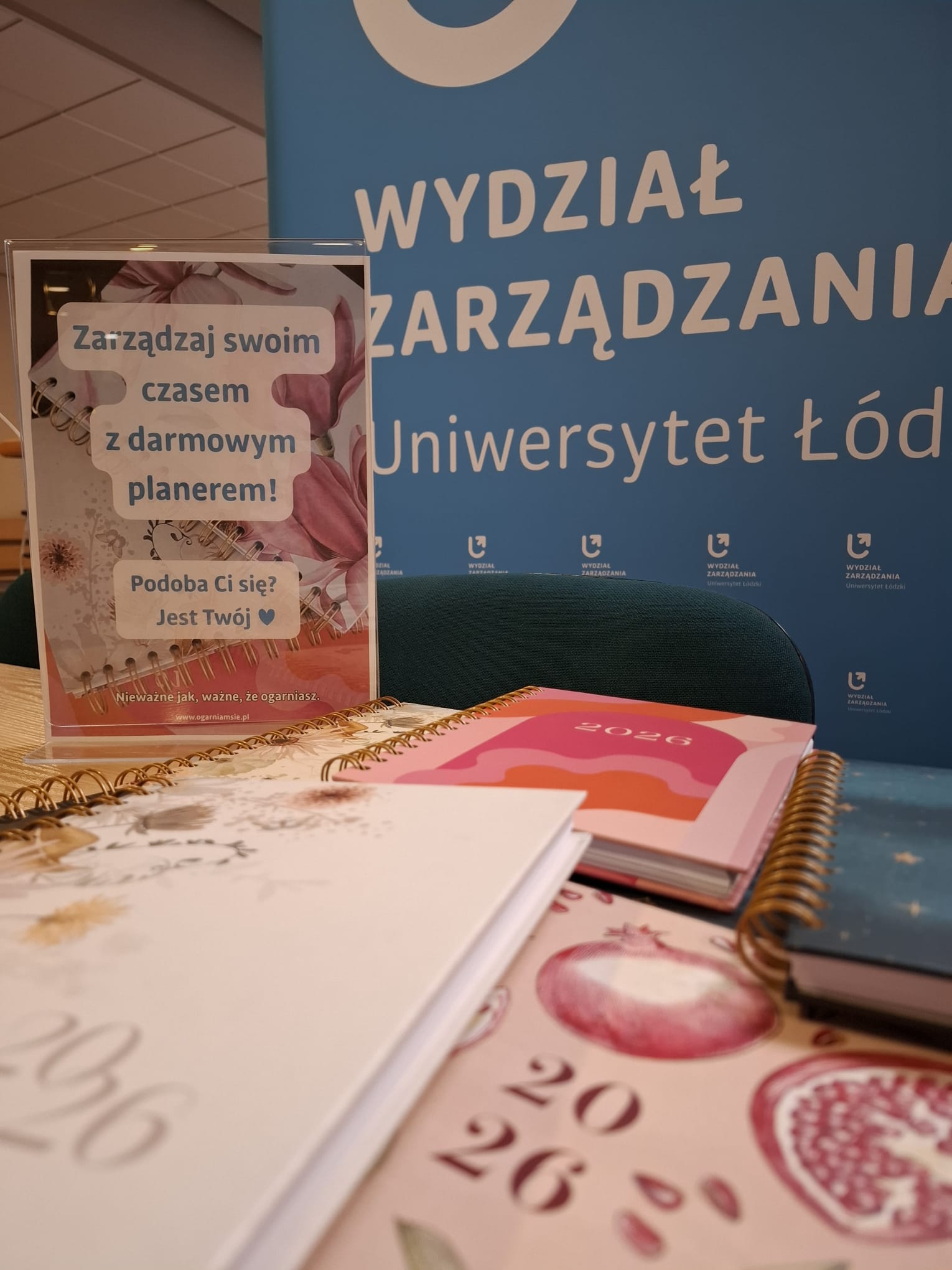 planery rozłożone na stole i kartka z informacją: Zarządzaj swoim czasem z bezpłatnym planerem. Podoba Ci się? Jest Twój.