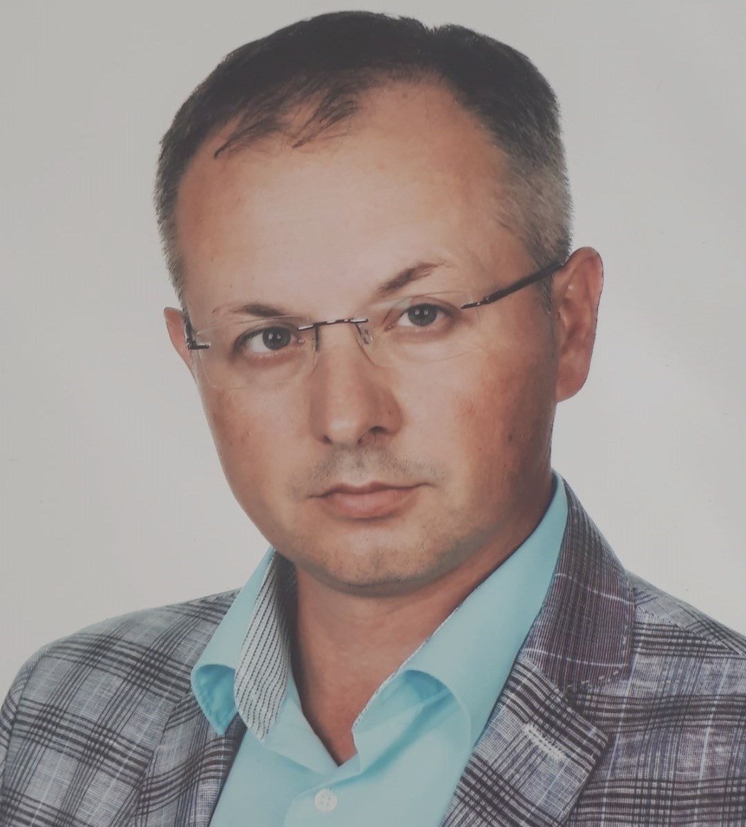 mężczyzna w okularach pozuje do zdjęcia w marynarce w kratkę