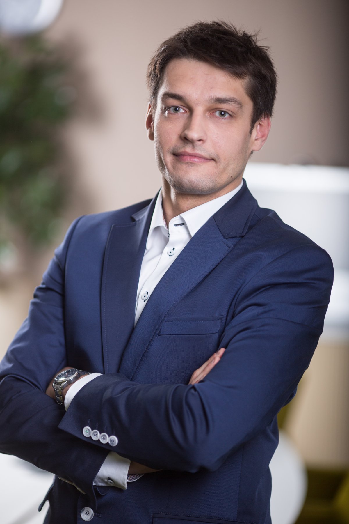 mężczyzna w garniturze stoi z rękoma założonymi, tło rozmyte