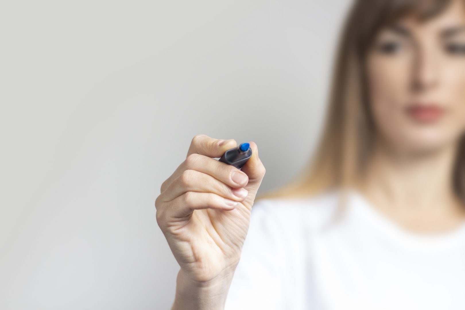 Young woman holds a blue marker and writes something on a light background. Banner Element dekoracyjny