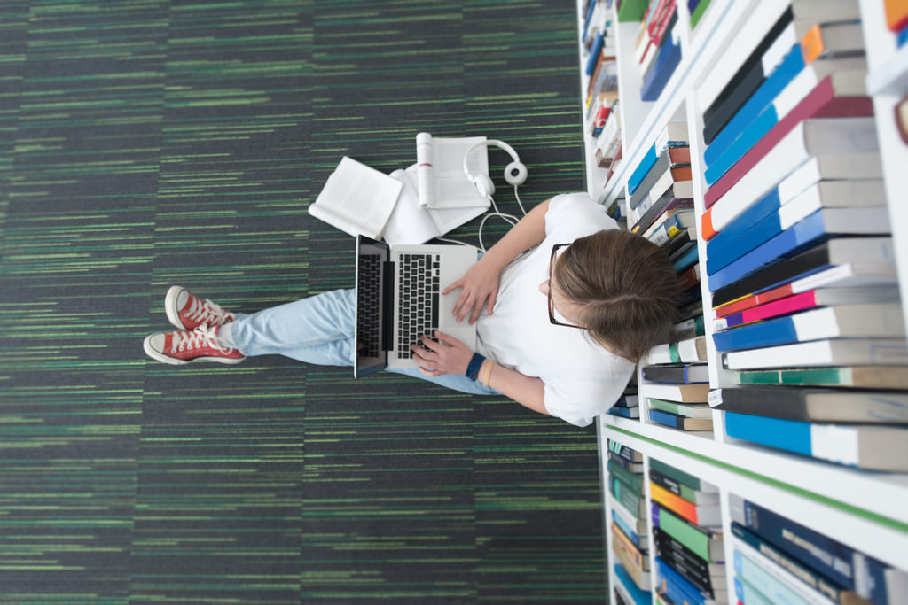 Osoba studiująca siedząca w bibliotece z komputerem