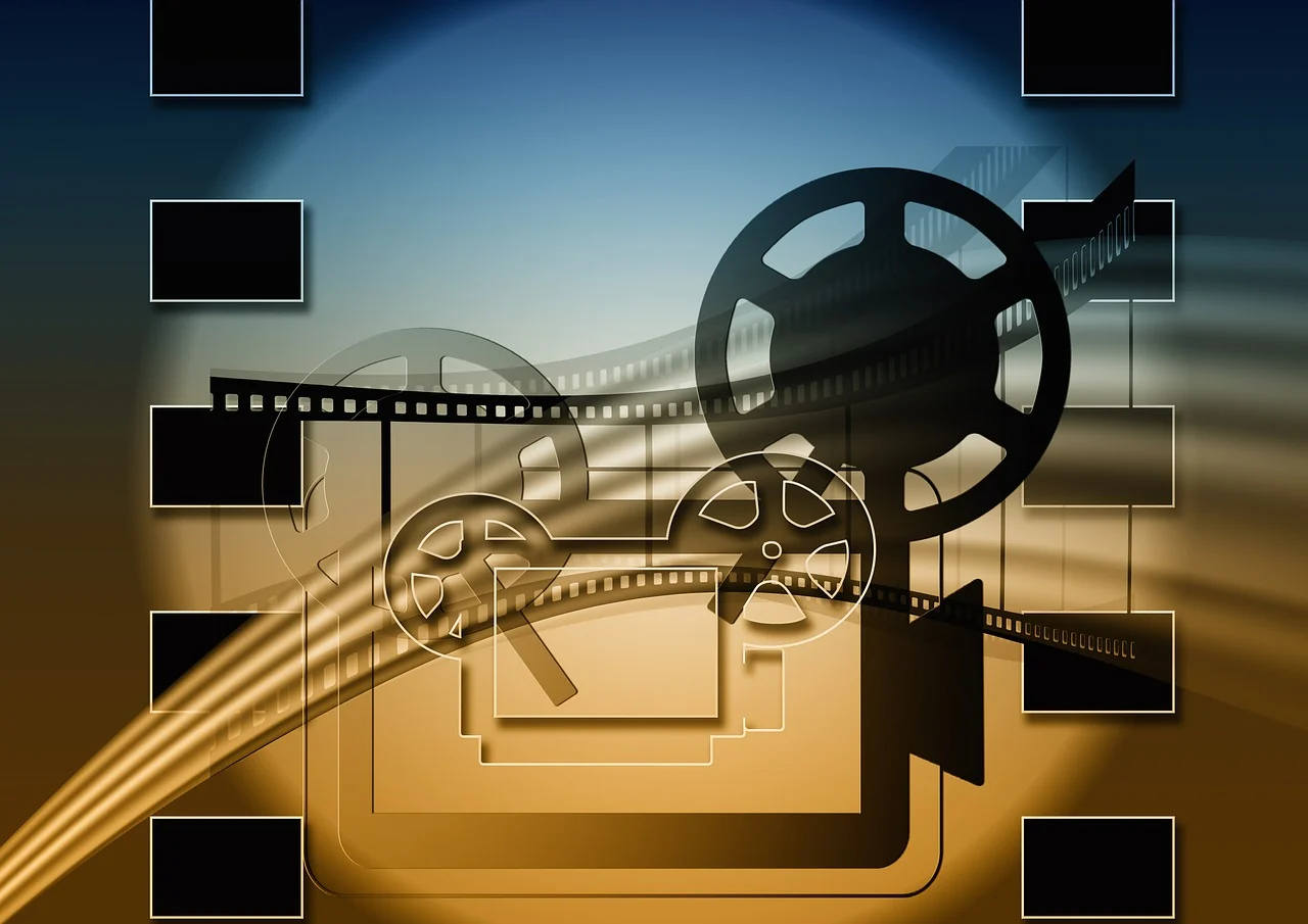Obraz przedstawia artystyczną grafikę związaną z kinematografią. W centralnej części widnieje sylwetka starego projektora filmowego z dużymi szpulami taśmy filmowej. Taśma filmowa przewija się przez całą kompozycję, tworząc dynamiczny efekt ruchu. 