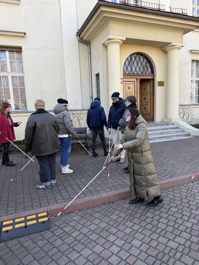 grupa ludzi z zasłoniętymi oczami, poruszająca się przy użyciu białej laski 